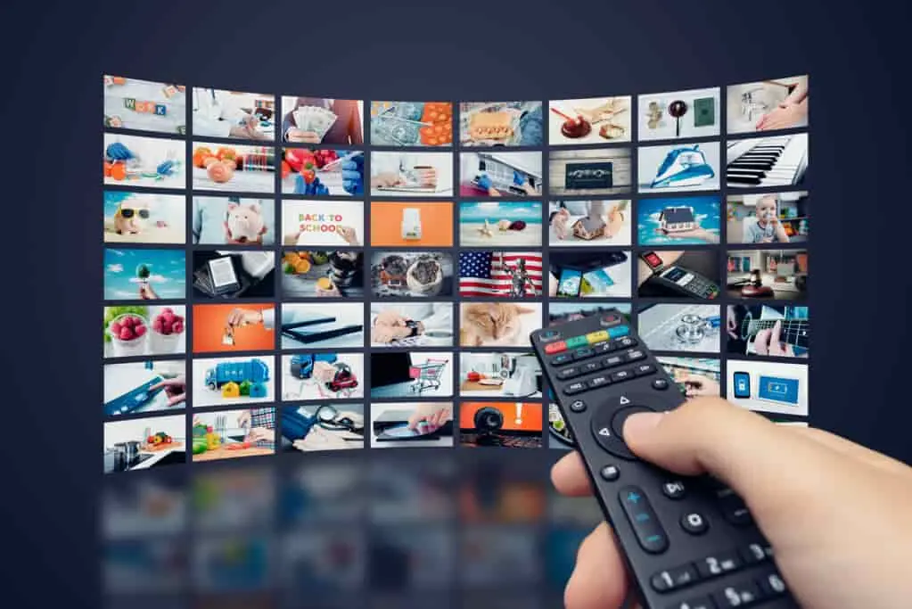 Hand holding a remote in front of a wall of live TV channels, illustrating what to look for in the best IPTV services